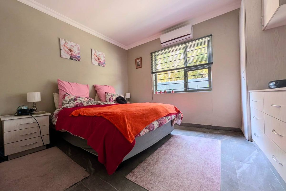 A well-maintained bedroom featuring built-in cupboards, tiled flooring, and a wall-mounted split-system air conditioner for climate control.