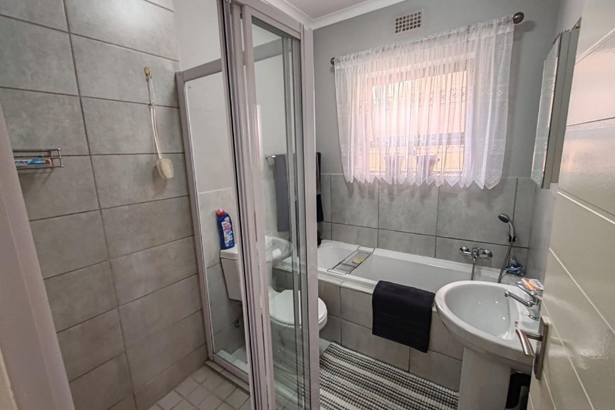 A functional bathroom featuring a glass-enclosed shower, a bathtub with a shower mixer, a pedestal basin, and neutral wall tiling.