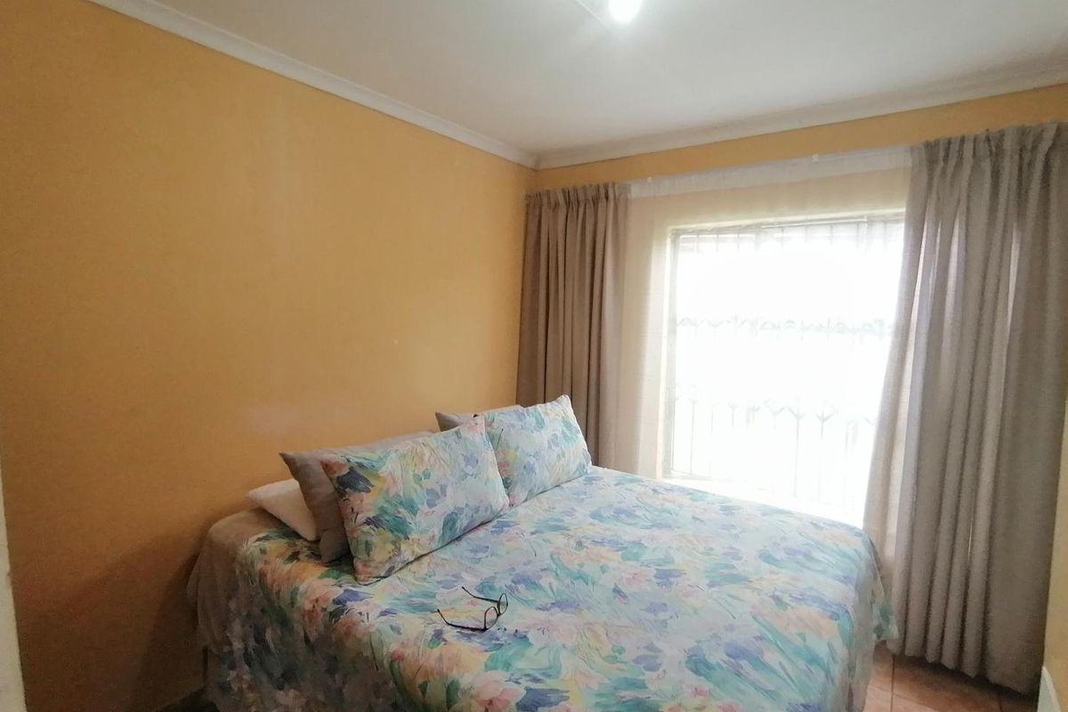 A standard bedroom featuring tiled flooring, a window with security bars, and neutral wall finishes.