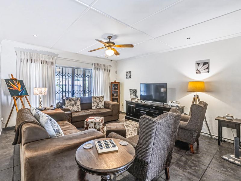 A comfortable living room featuring tiled flooring, a ceiling fan, and large windows with security gates, providing a functional and well-lit space.