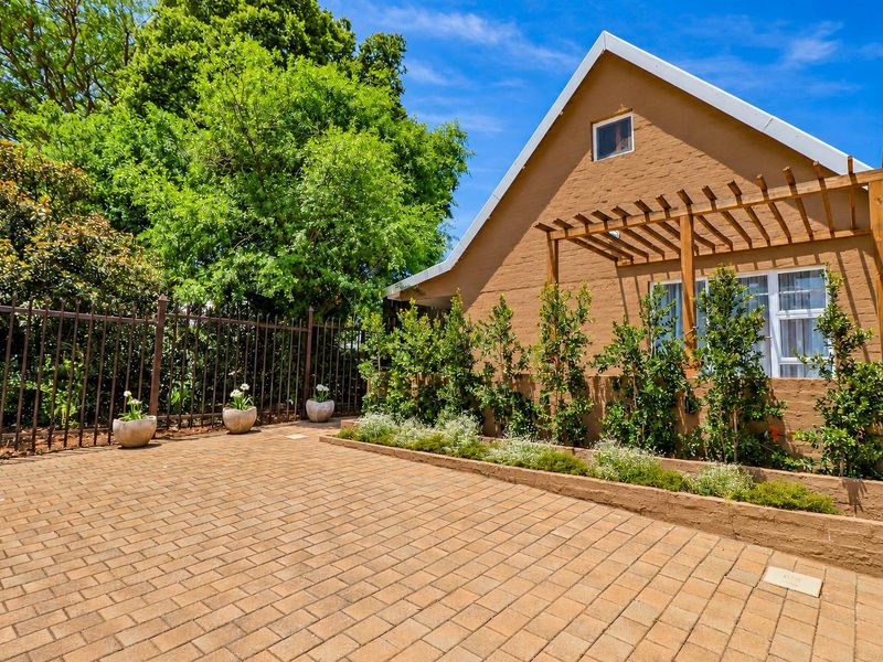 A well-maintained rear exterior area featuring brick paving, a timber pergola, and a raised garden bed against a brick facade.