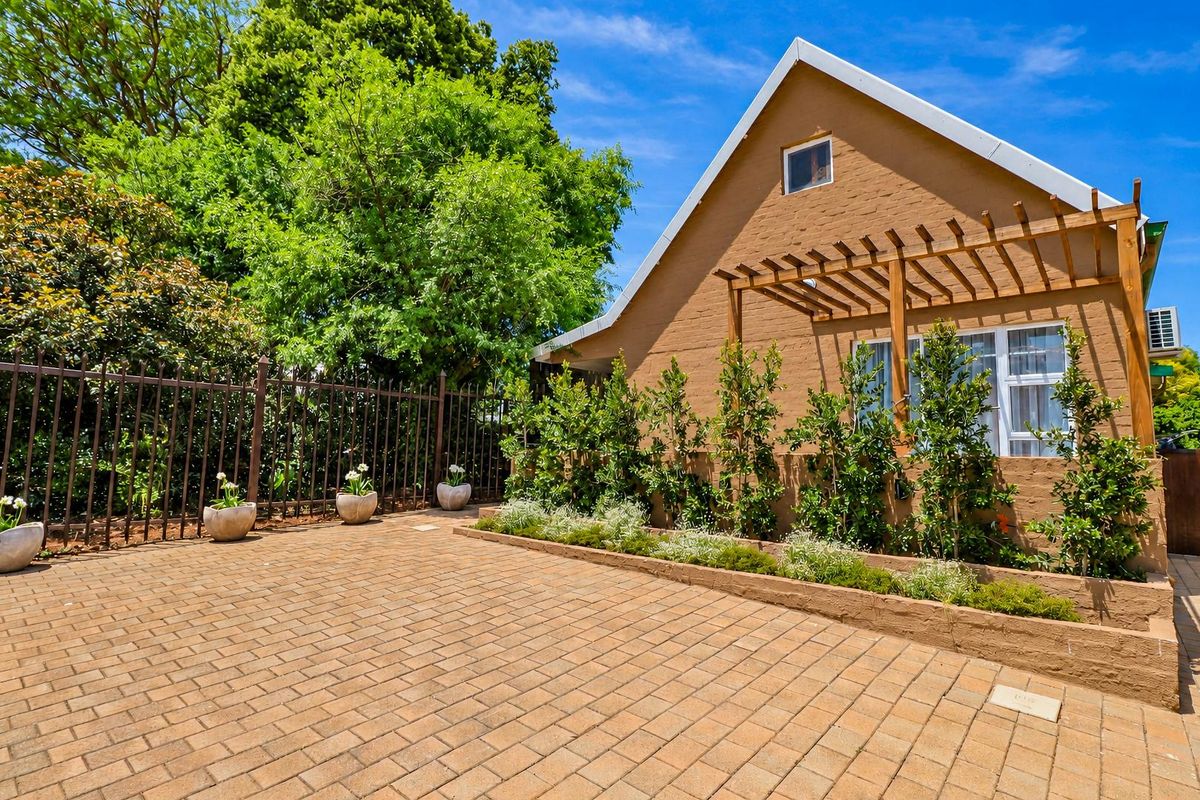 A well-maintained rear exterior area featuring brick paving, a timber pergola, and a raised garden bed against a brick facade.