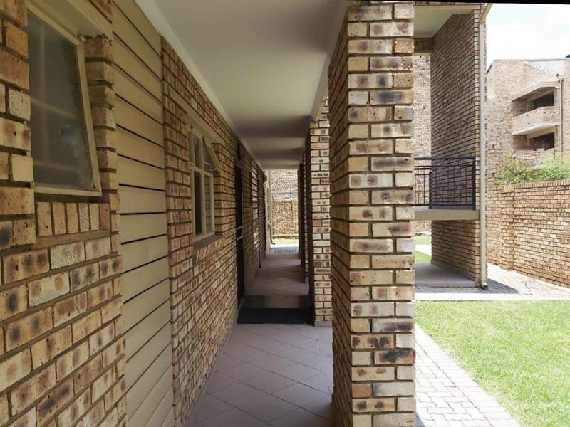 A covered exterior walkway featuring face brick construction and tiled flooring, providing access to apartment units within the complex.