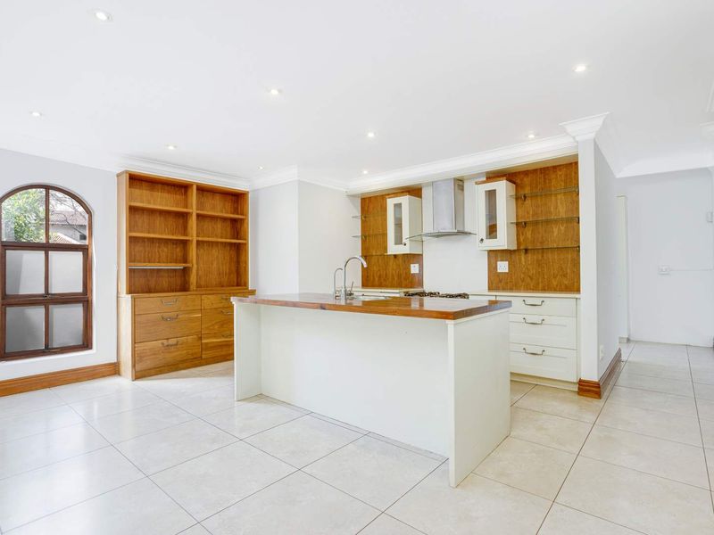 A bright, open-plan kitchen featuring a central island, built-in wooden cabinetry, an extractor fan, and an elegant arched window with tiled flooring throughout.