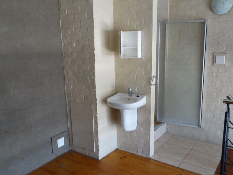 A compact bathroom area featuring a pedestal washbasin, shower enclosure, and a mix of timber and tiled flooring, requiring cosmetic updates.