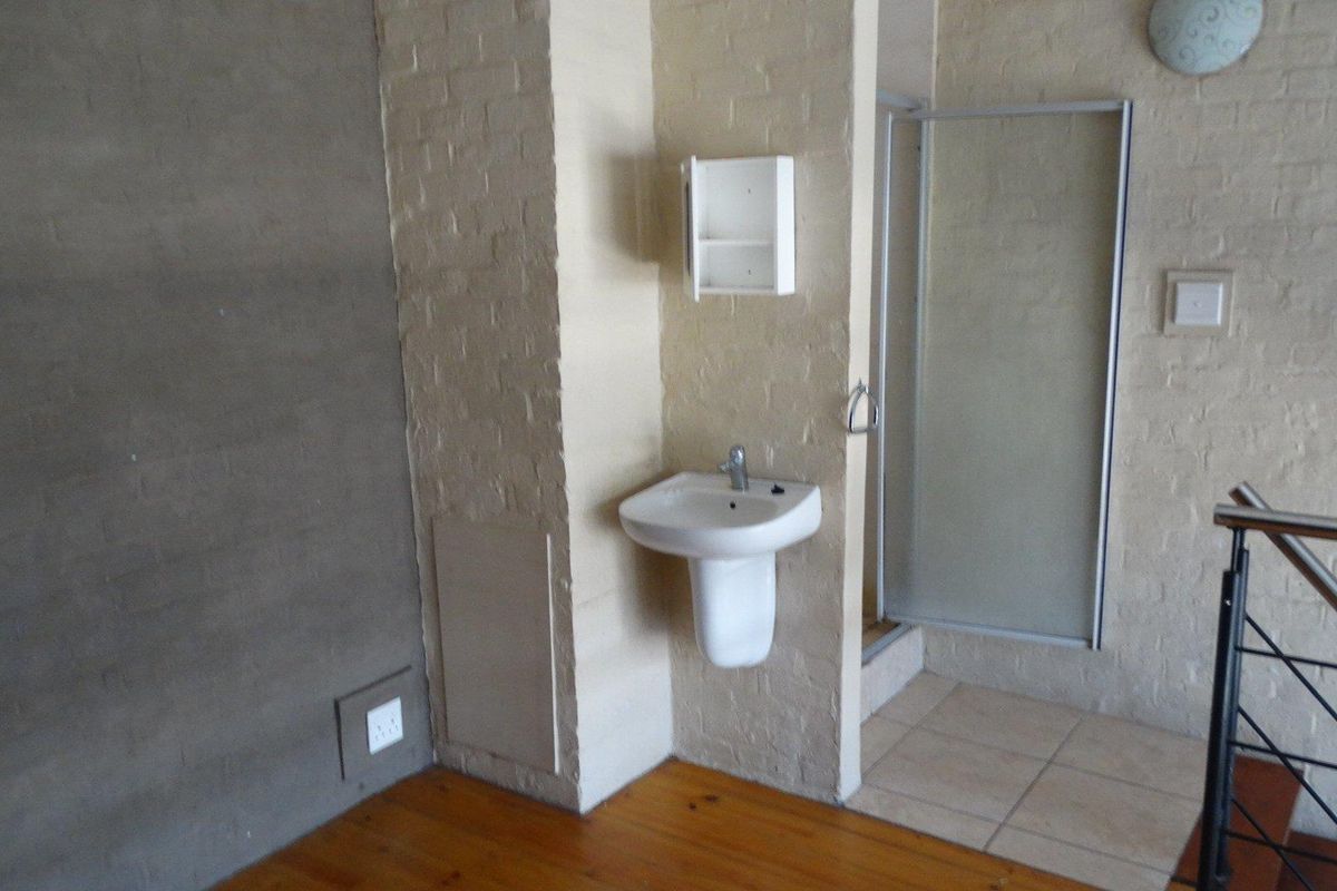 A compact bathroom area featuring a pedestal washbasin, shower enclosure, and a mix of timber and tiled flooring, requiring cosmetic updates.