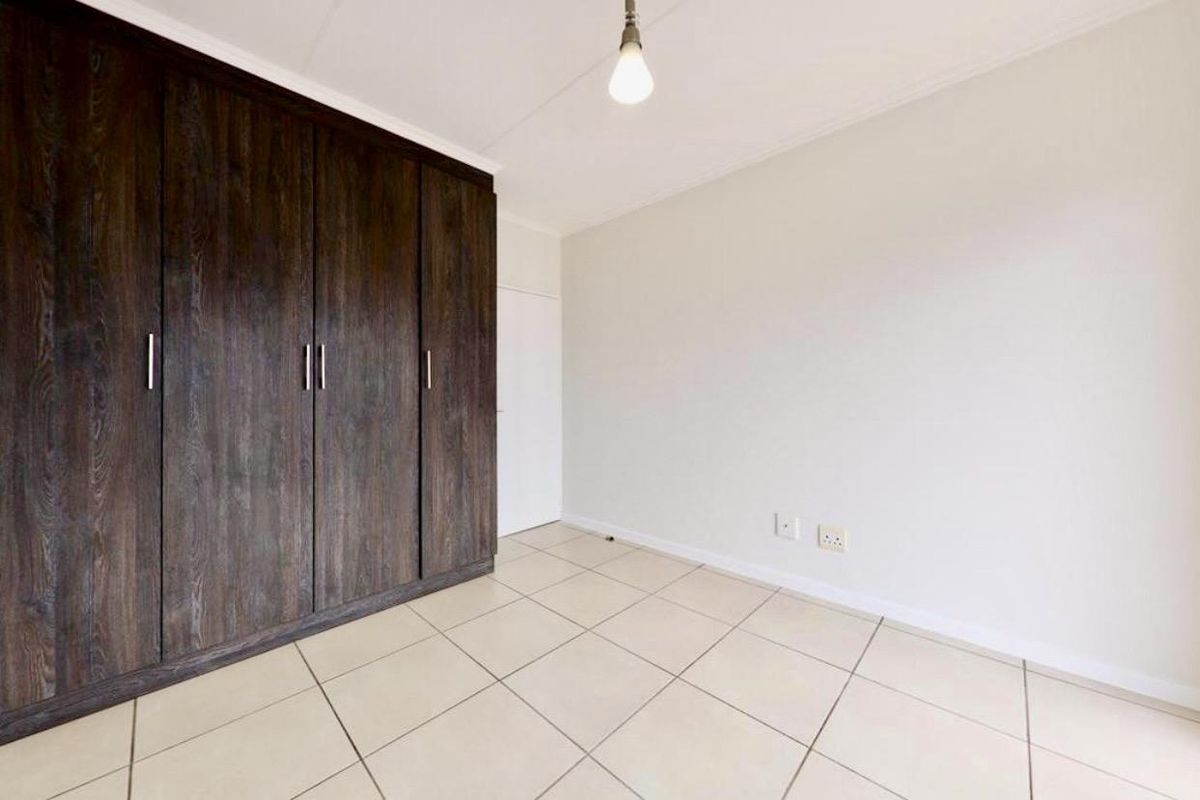 A bright, empty bedroom featuring neutral floor tiles and dark wood-finish built-in cupboards.