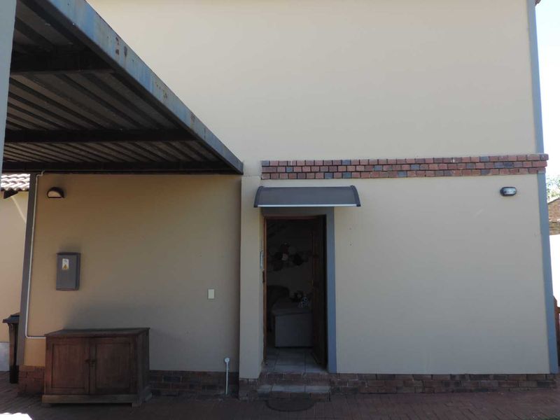 Rear exterior view of the property featuring a paved patio area, a metal carport, and a doorway with a protective canopy.
