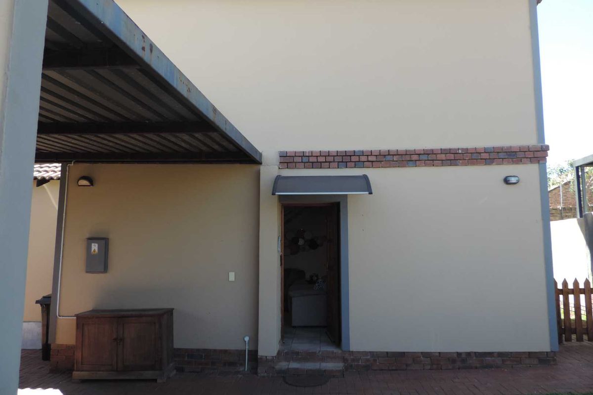 Rear exterior view of the property featuring a paved patio area, a metal carport, and a doorway with a protective canopy.
