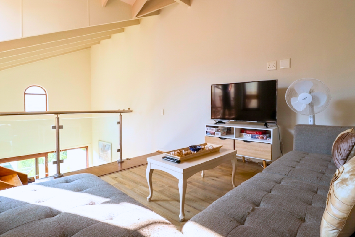 A cozy loft-style living area featuring vaulted ceilings with exposed rafters, laminate flooring, and a modern glass balustrade overlooking the lower level.