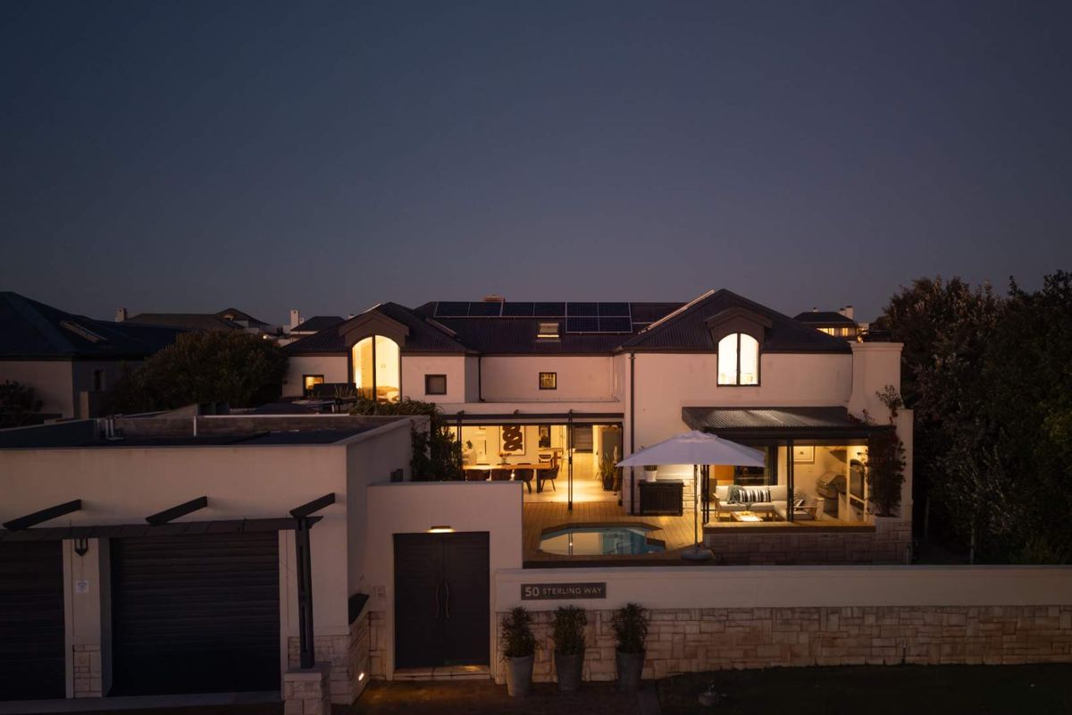 An aerial evening view of the rear property featuring a swimming pool, wooden decking, covered patio area, and solar panels on the roof.