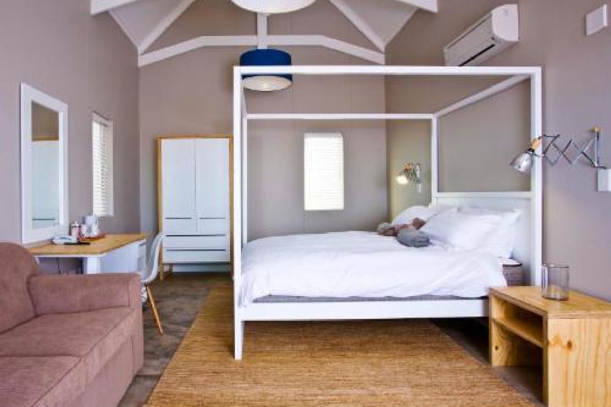Spacious bedroom featuring a vaulted ceiling with exposed beams, polished concrete flooring, and a wall-mounted air conditioning unit.