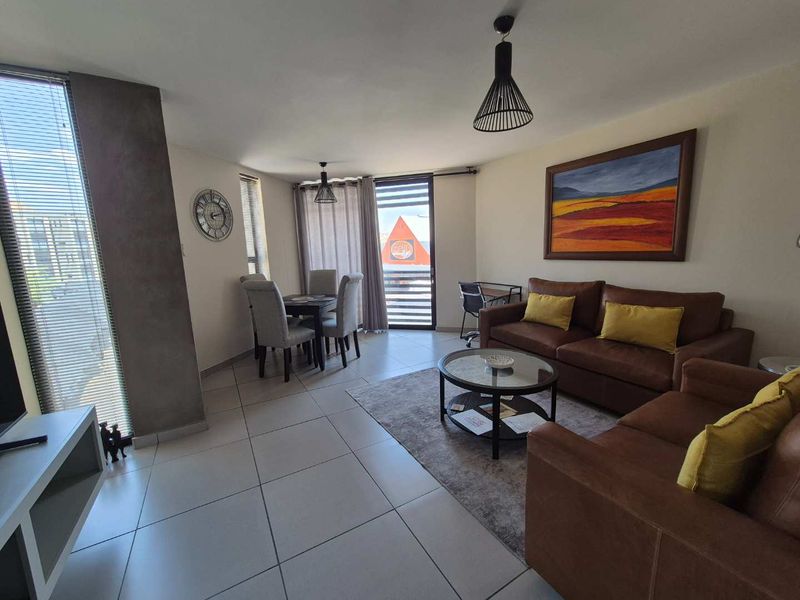 An open-plan living and dining area featuring tiled flooring, modern pendant lighting, and access to a balcony through a sliding door.