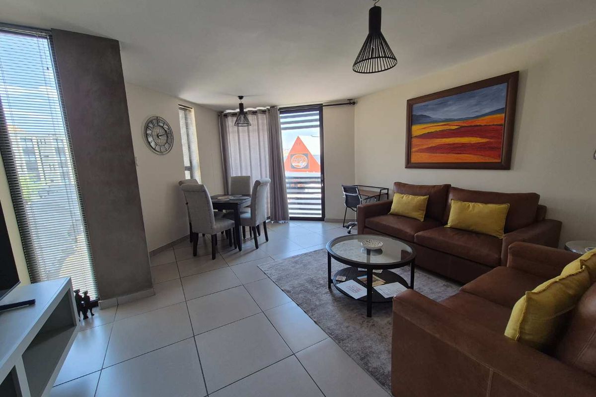 An open-plan living and dining area featuring tiled flooring, modern pendant lighting, and access to a balcony through a sliding door.