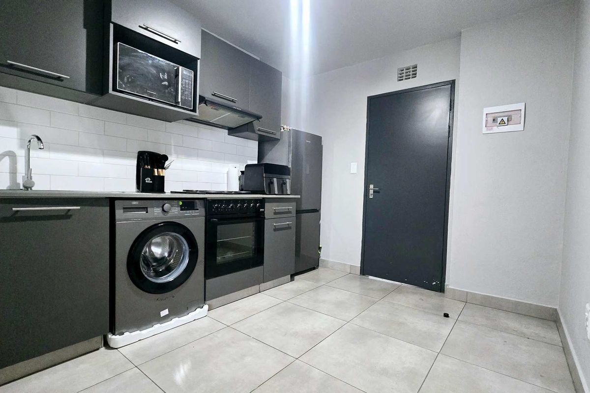 Modern kitchen featuring dark grey cabinetry, subway tile backsplash, integrated oven, extractor fan, and built-in microwave with neutral tiled flooring.