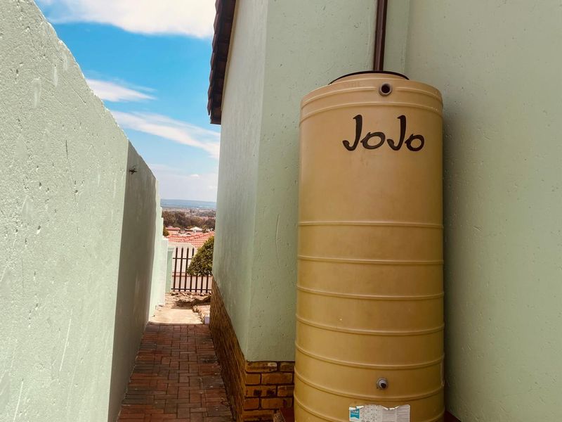 A side passage featuring a water storage tank installed against the exterior wall with brick paving leading towards the rear of the property.
