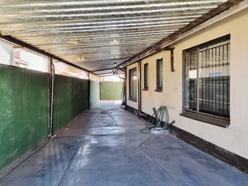 A covered outdoor driveway or carport area featuring a corrugated metal roof, concrete flooring, and perimeter walling with security window bars.