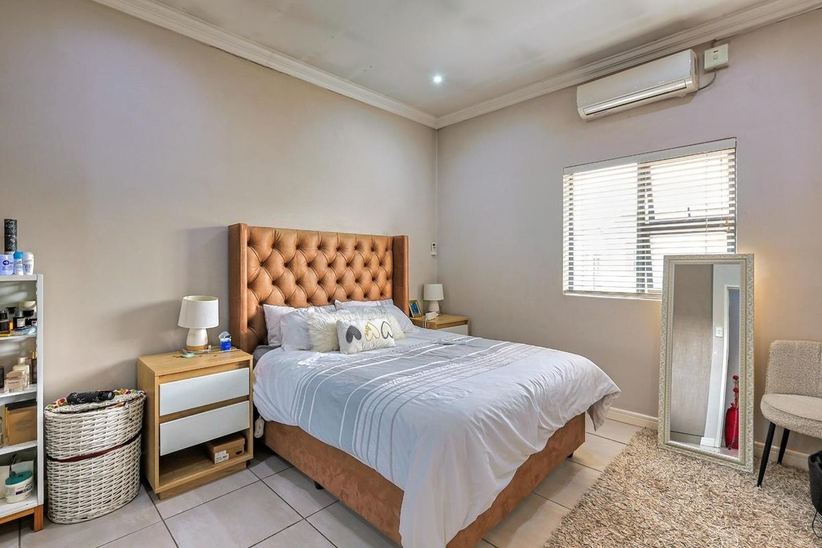 A well-lit bedroom featuring tiled flooring, a wall-mounted air conditioning unit, and a window with fitted blinds.