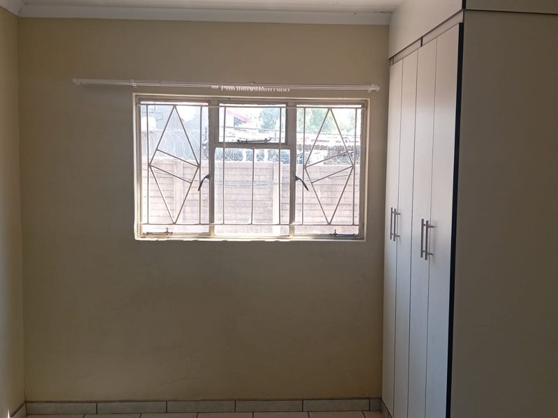 A simple, empty bedroom featuring tiled flooring, a built-in wardrobe, and a window fitted with security bars.