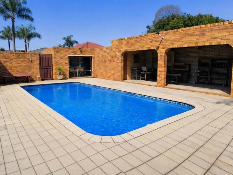 Outdoor pool area featuring a paved patio and a covered entertainment space with a built-in braai, enclosed by brick boundary walls.
