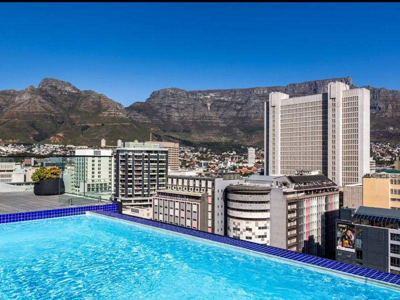 A stunning rooftop infinity pool featuring a glass balustrade and panoramic views of the city and Table Mountain.