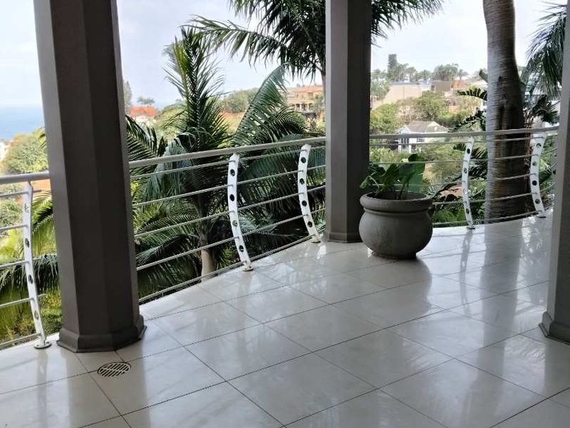 A spacious covered balcony featuring tiled flooring, structural columns, and a metal balustrade, offering scenic outdoor views.