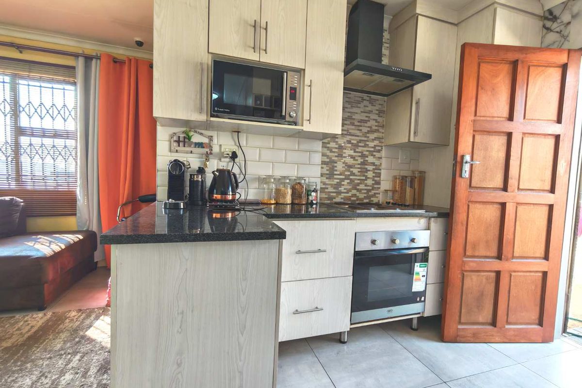 Compact kitchen featuring light wood-grain cabinetry, granite countertops, subway tile backsplash, and integrated appliances including an oven and extractor fan.