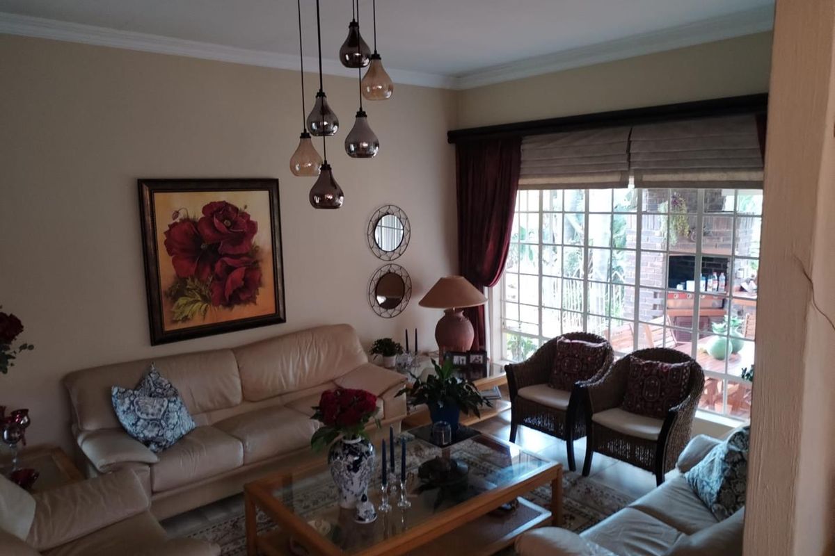 A comfortable living room featuring a large window with garden views, crown molding, and a modern multi-pendant light fixture.