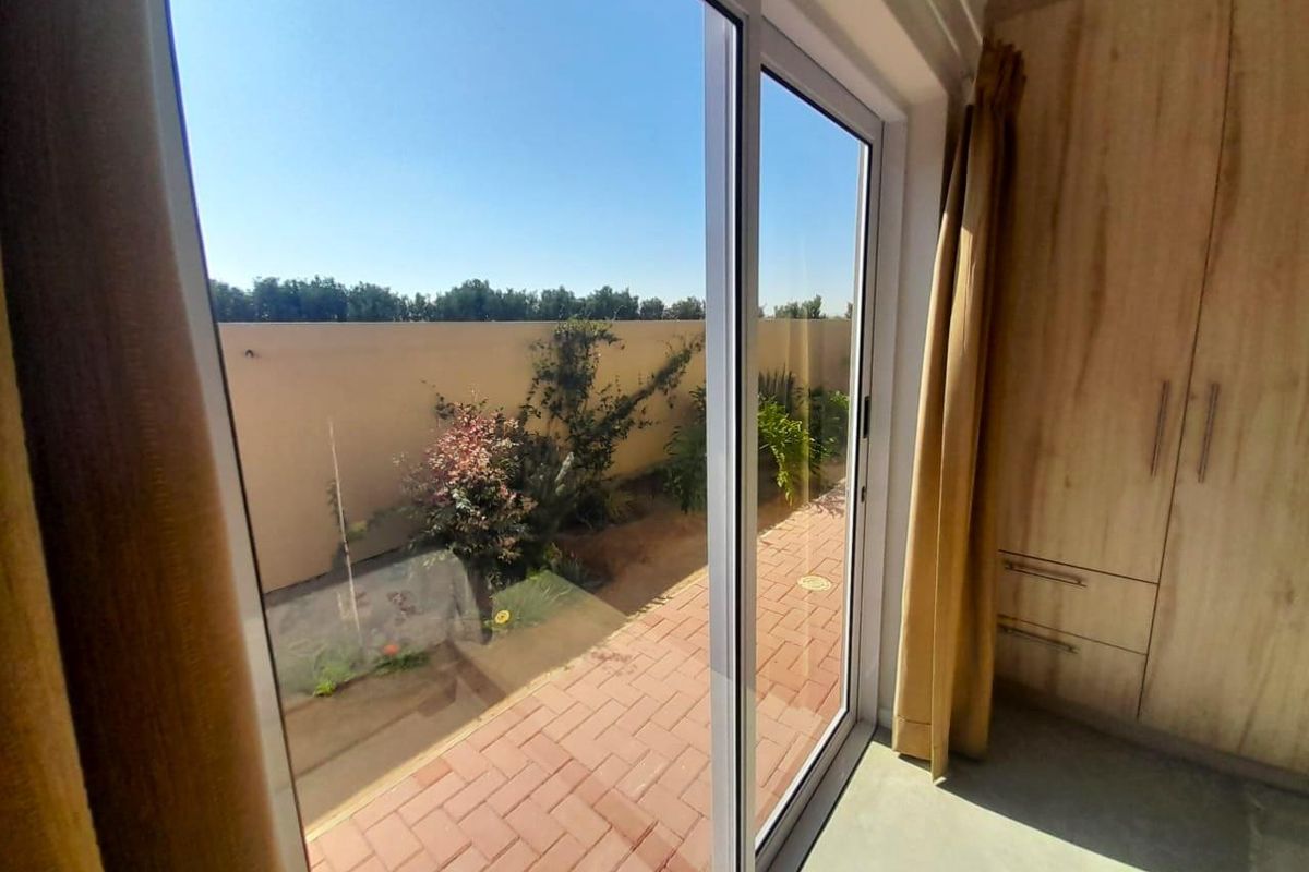 A view from a bedroom featuring built-in wooden cabinetry and sliding glass doors opening onto a paved patio and garden area.
