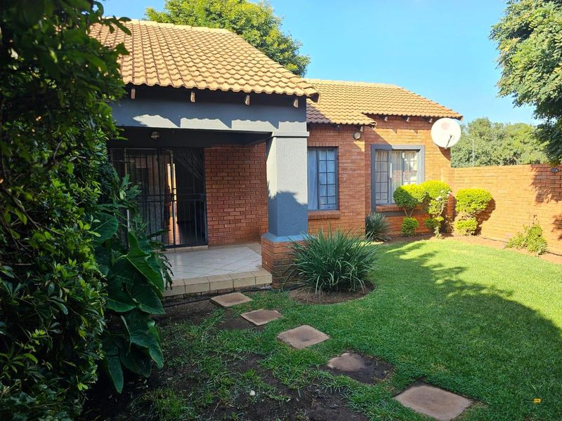 Rear view of the townhouse featuring a face-brick facade, a covered patio area, and a well-maintained private garden with paved walkway.