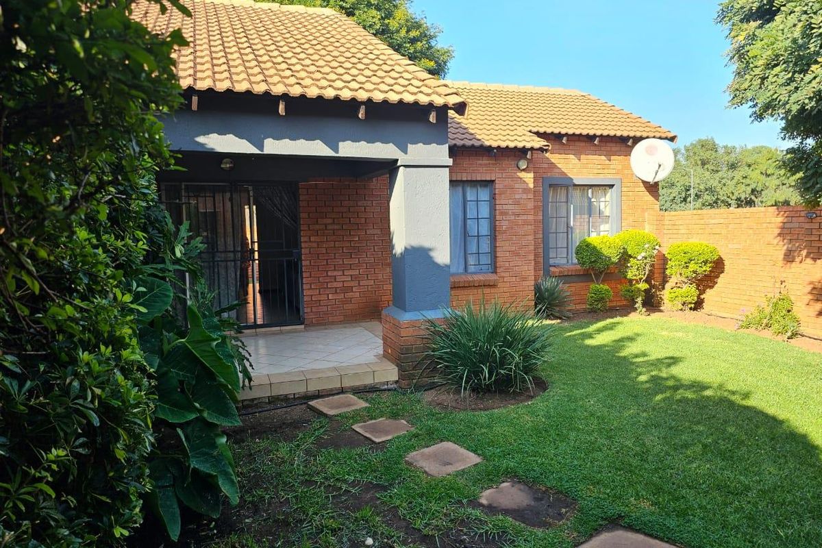 Rear view of the townhouse featuring a face-brick facade, a covered patio area, and a well-maintained private garden with paved walkway.