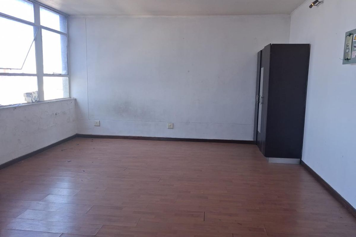 An empty bedroom featuring laminate flooring and a large window, requiring cosmetic updates to the walls and paintwork.