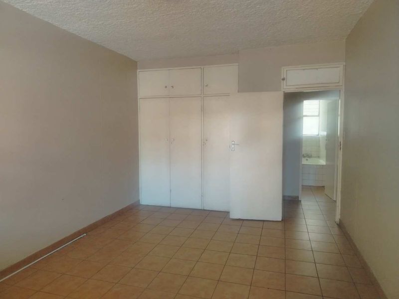 An empty bedroom featuring tiled flooring, built-in cupboards, and a textured ceiling, with an adjacent view into a bathroom area.