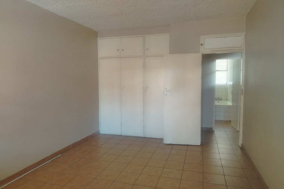An empty bedroom featuring tiled flooring, built-in cupboards, and a textured ceiling, with an adjacent view into a bathroom area.