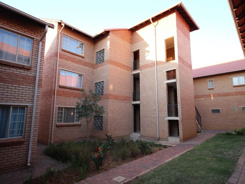 Exterior view of a multi-story apartment complex featuring face brick construction, tiled roofing, and a landscaped courtyard with paved walkways.