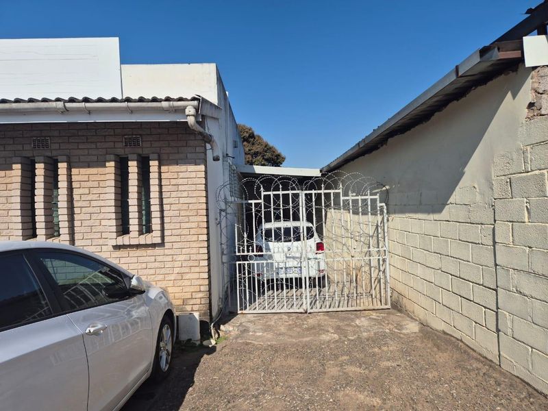 Exterior view of the property entrance featuring a brick facade, concrete driveway, and a secured gate with razor wire.
