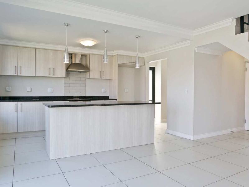 Modern open-plan kitchen featuring light wood cabinetry, granite countertops, and tiled flooring, seamlessly integrated with the living area and staircase.