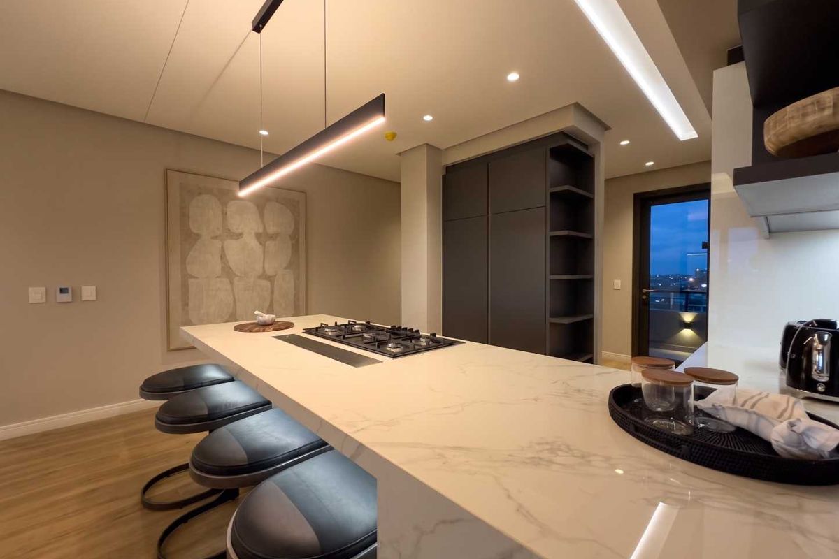 Modern kitchen featuring a large stone-topped island with a built-in gas hob, sleek cabinetry, and contemporary recessed and pendant lighting.