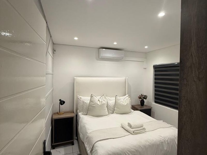 A modern, well-maintained bedroom featuring tiled flooring, recessed downlighting, and a wall-mounted split-system air conditioning unit.