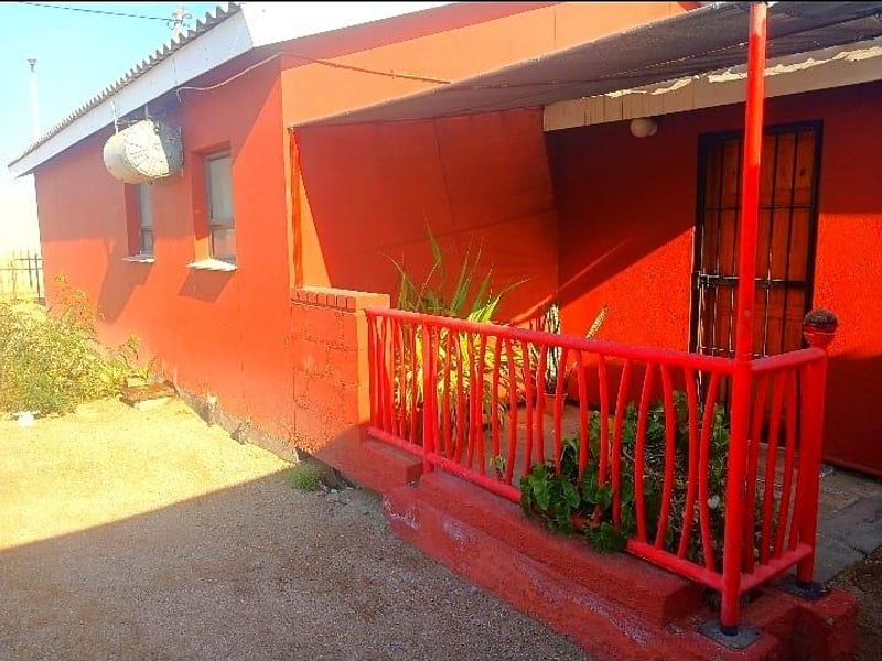 A covered patio area featuring a metal security gate, red painted railings, and a shade cloth awning, showing signs of exterior wear.
