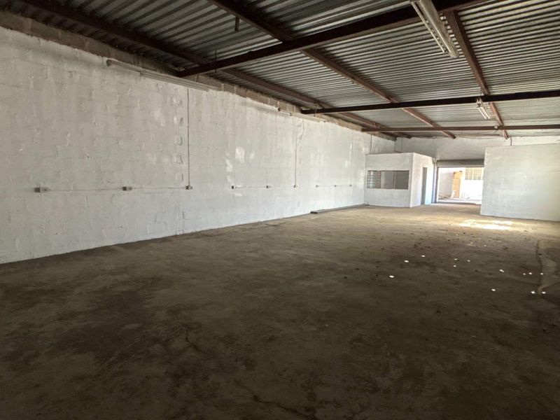 Spacious industrial utility area featuring exposed steel roof trusses, concrete flooring, and painted masonry walls, suitable for storage or workshop use.