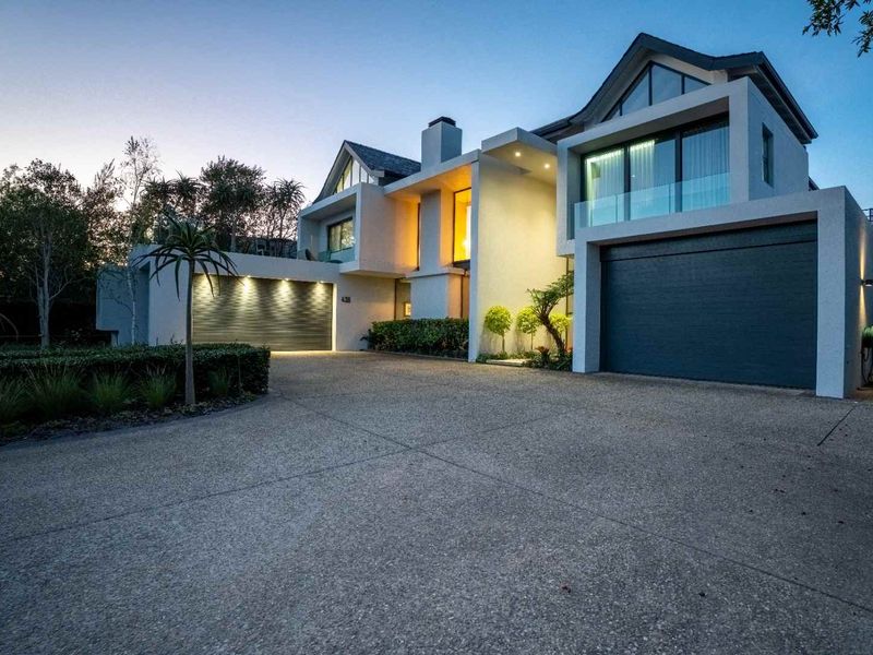 Modern architectural residence featuring a spacious concrete driveway, double garage, and striking contemporary facade with integrated exterior lighting.