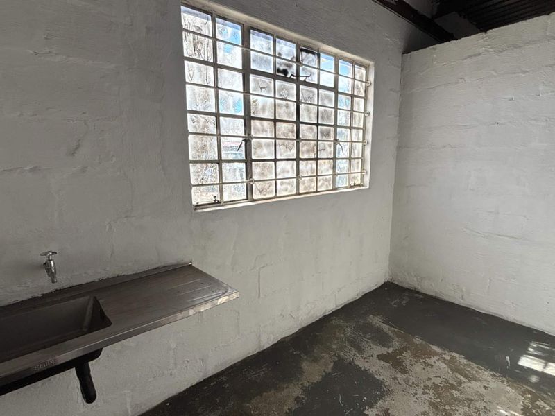 A functional industrial utility space featuring a stainless steel sink, painted masonry walls, and a large steel-framed window with concrete flooring.
