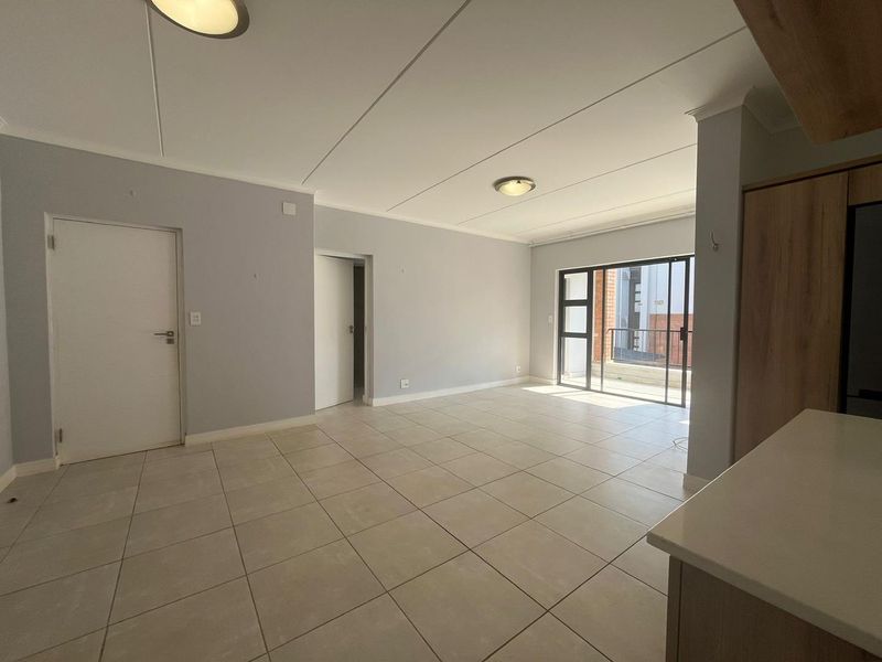 A bright, open-plan living area featuring neutral tiled flooring, clean walls, and a sliding glass door leading to an outdoor space.