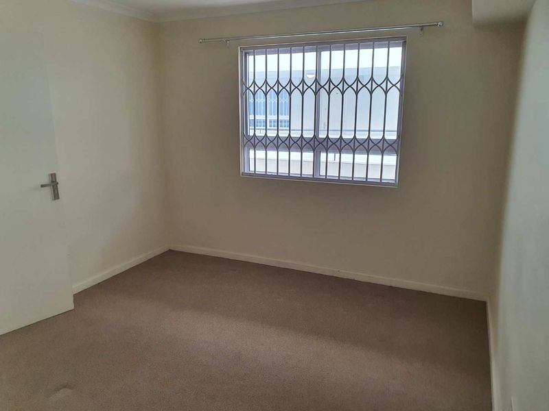 A vacant bedroom featuring neutral walls, carpeted flooring, and a window fitted with a security gate and curtain rod.