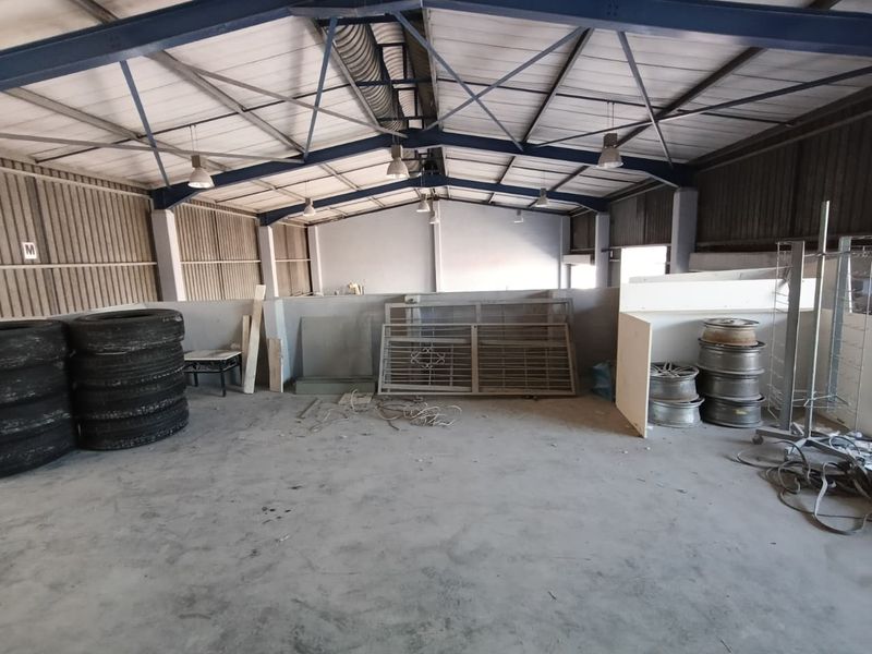 Spacious industrial utility area featuring exposed steel roof trusses, concrete flooring, and high-clearance walls suitable for storage or workshop operations.