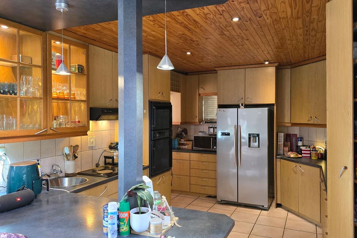 A functional kitchen featuring wood-finish cabinetry, built-in oven, integrated hob, and tiled flooring, offering a traditional layout with ample storage space.