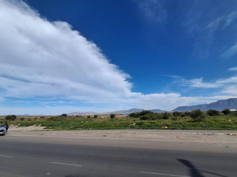 A wide-angle view of an undeveloped agricultural land parcel adjacent to a paved road with distant mountain scenery.