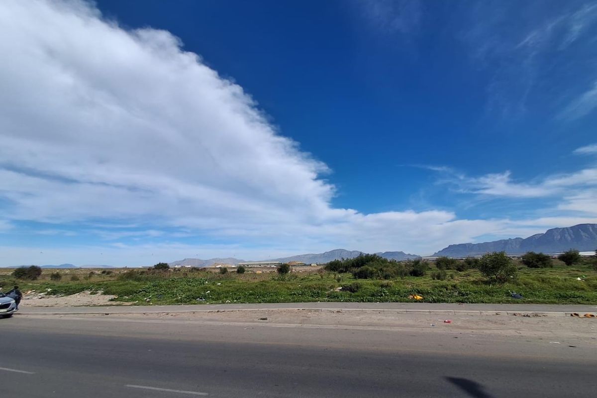 A wide-angle view of an undeveloped agricultural land parcel adjacent to a paved road with distant mountain scenery.