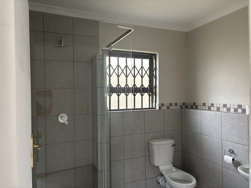 A clean and functional bathroom featuring a walk-in shower with glass screen, tiled walls, and a security gate on the window.